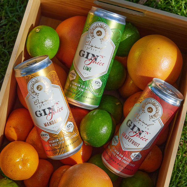 All flavours of Gin N Juice cans sitting in a crate surrounded by mandarins, limes and grapefruits.