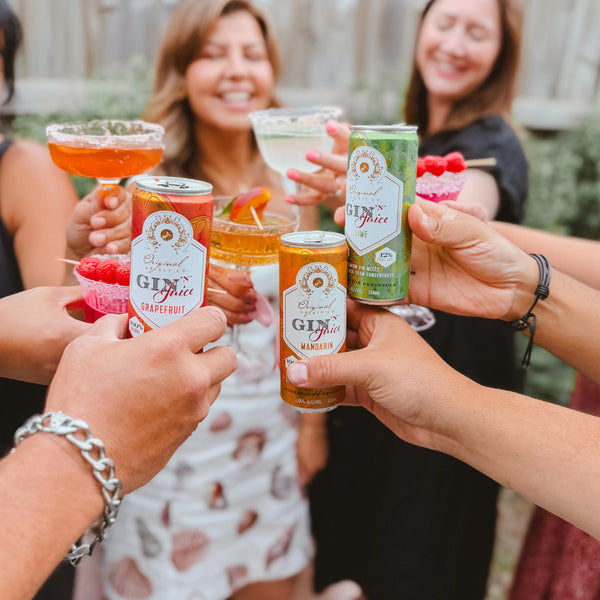 People celebrating with cans of 'Gin N Juice' and others holding cocktails with garnishes in an outdoor setting.