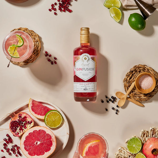 Bottle of Ruby Grapefruit Ginfusion gin surrounded by garnishes and cocktails on a light surface