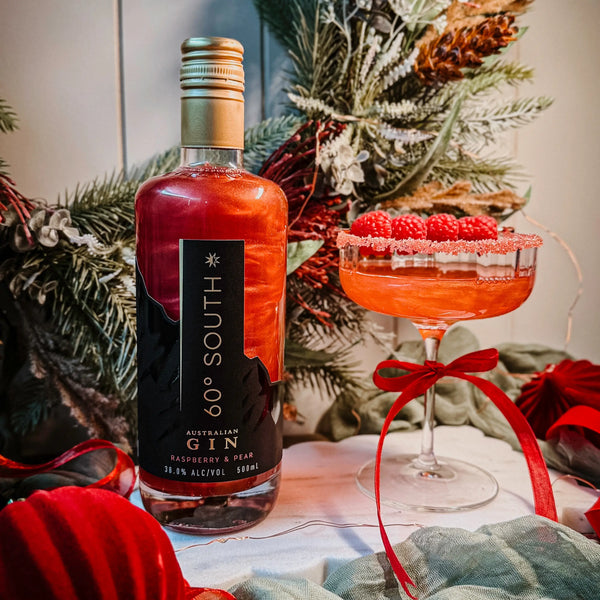 Red Raspberry and Pear 60º Degree South Gin and a cocktail garnished with Raspberries and a red ribbon, set against a Christmas background.