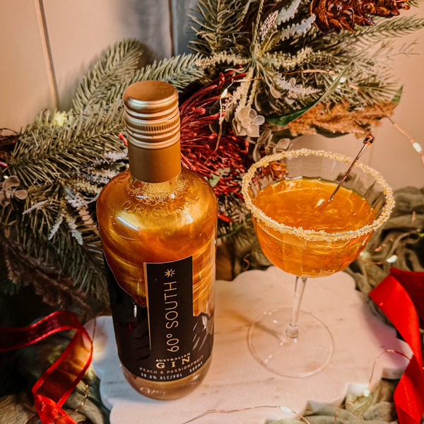 Bottle of 60° South Yellow Glitter Gin and a cocktail glass with a drink in front of a Christmas themed setting.
