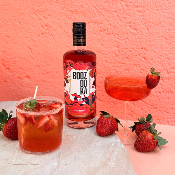 Bottle of Boozooka Strawberry Vodka with two cocktails and strawberries on a pink background