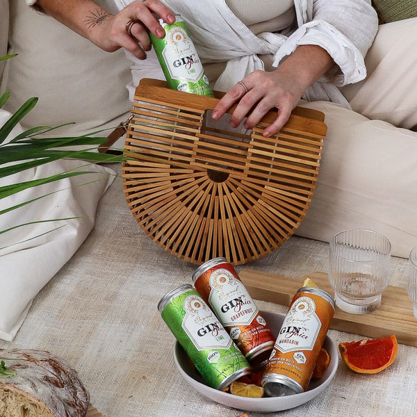 Person holding a wooden handbag with Gin N Juice cans and a glass on a serving tray.