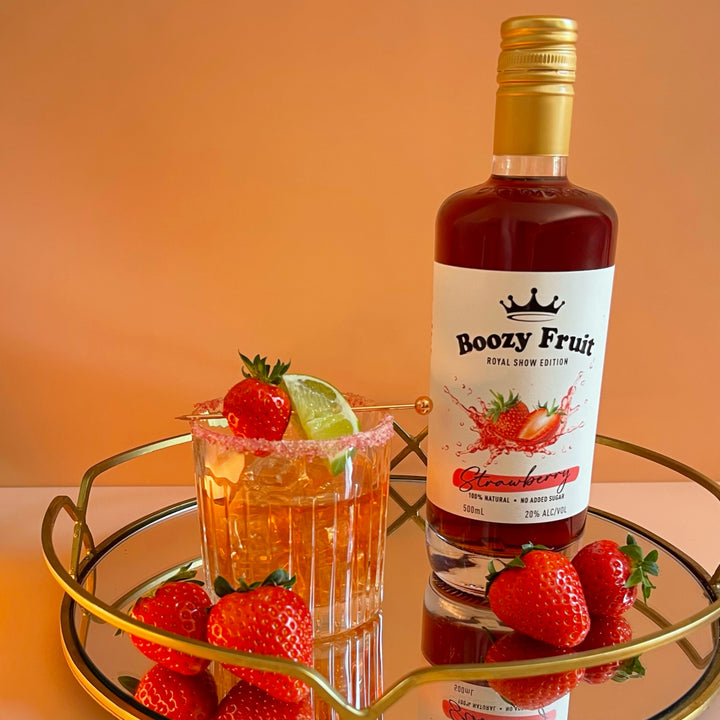 A bottle of Boozy Fruit Strawberry Vodka made into a cocktail surrounded by fresh strawberries, showcasing its vibrant red hue.