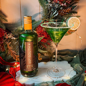 Bottle of 60 South Green Aple and Lime  Glitter Gin with a green cocktail garnished with a lime wedge, set against a festive background.